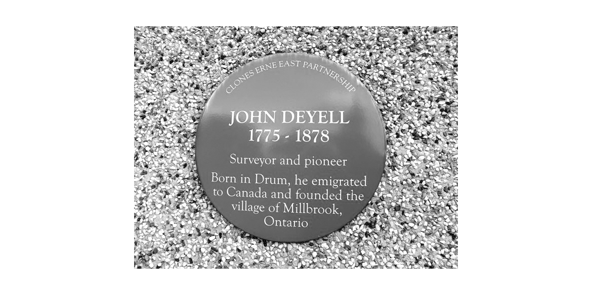 Circular commemorative plaque on gravel: 'John Deyell 1775–1878' with text about a surveyor and pioneer and the village of Millbrook, Ontario.