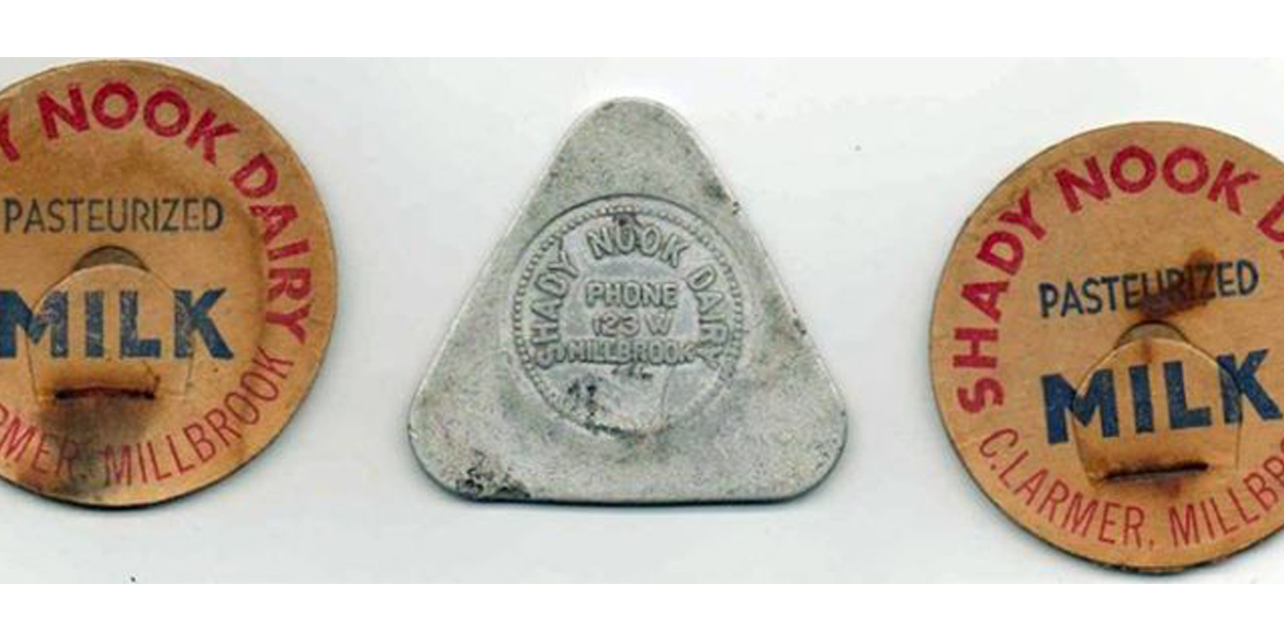 Three dairy bottle caps: two orange round lids reading 'Shady Nook Dairy' and 'Milk' with 'Pasteurized' text, flanking a silver triangular cap in the center.