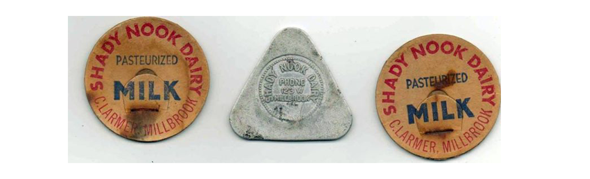 Three dairy bottle caps: two orange round lids reading 'Shady Nook Dairy' and 'Milk' with 'Pasteurized' text, flanking a silver triangular cap in the center.
