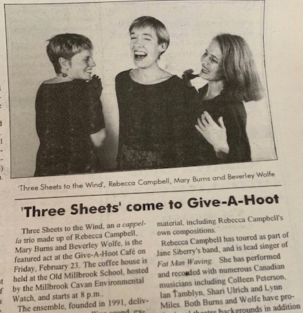 Three women in black outfits smiling and chatting in a newspaper photo.